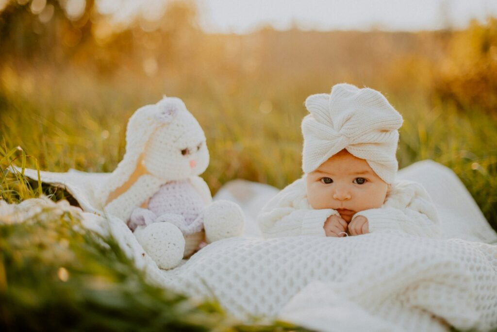 a baby lying in grass with a stuffed animal